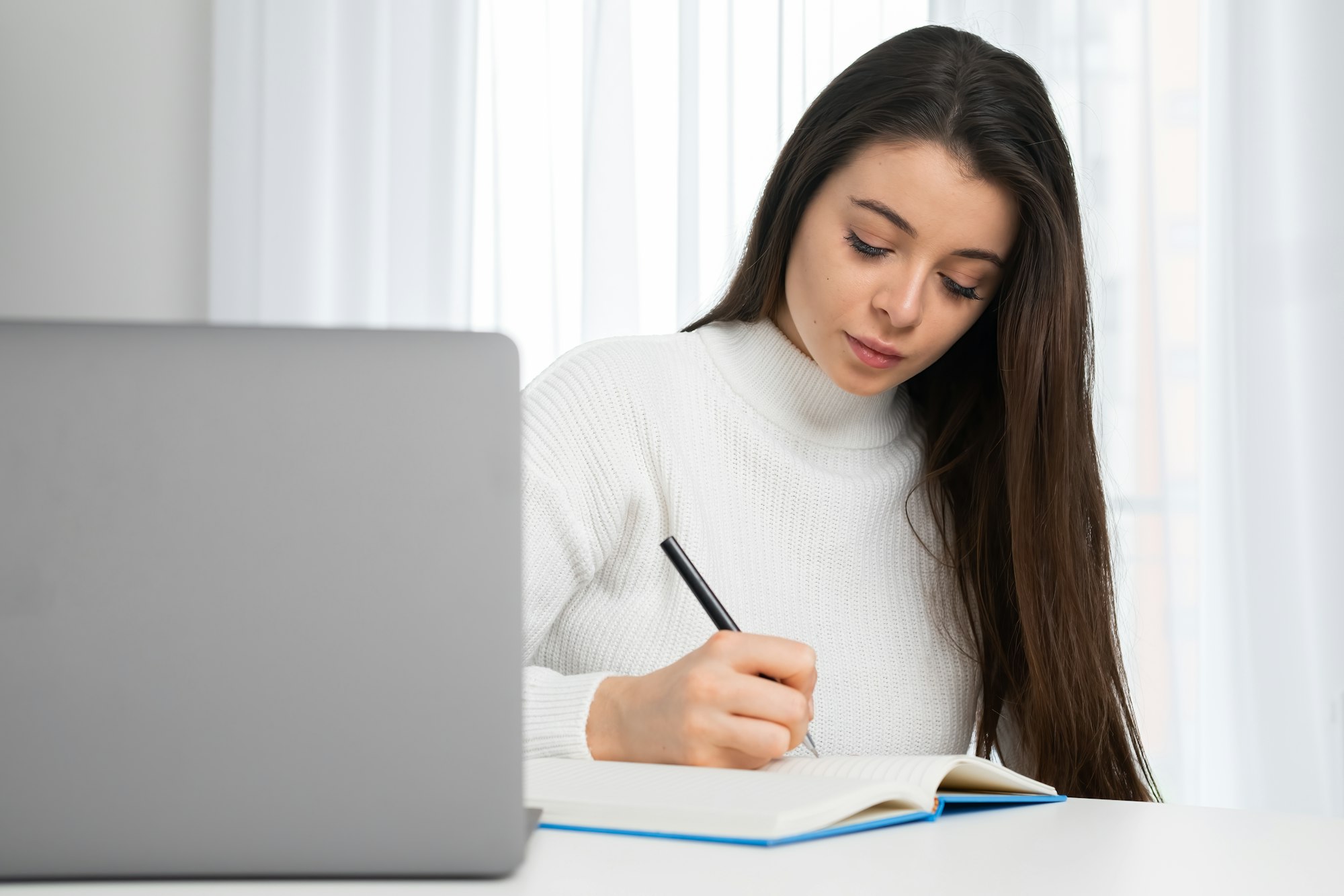 Young woman takes online courses via notebook making notes